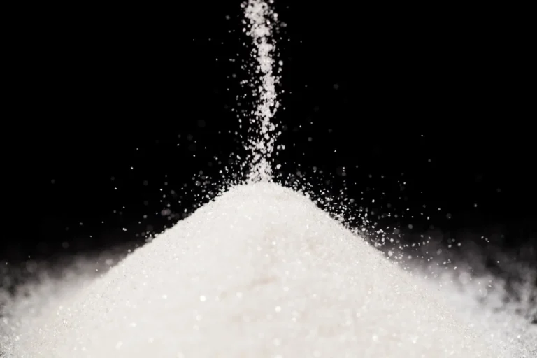 Granulated sugar falling into pile against black background.